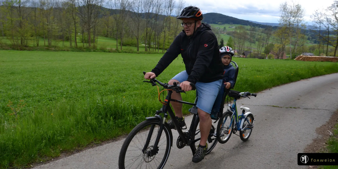 Mann auf Fahrrad mit Kind im Fahrradkindersitz und Kinderfahrrad im Schlepptau angehängt mit foaweida